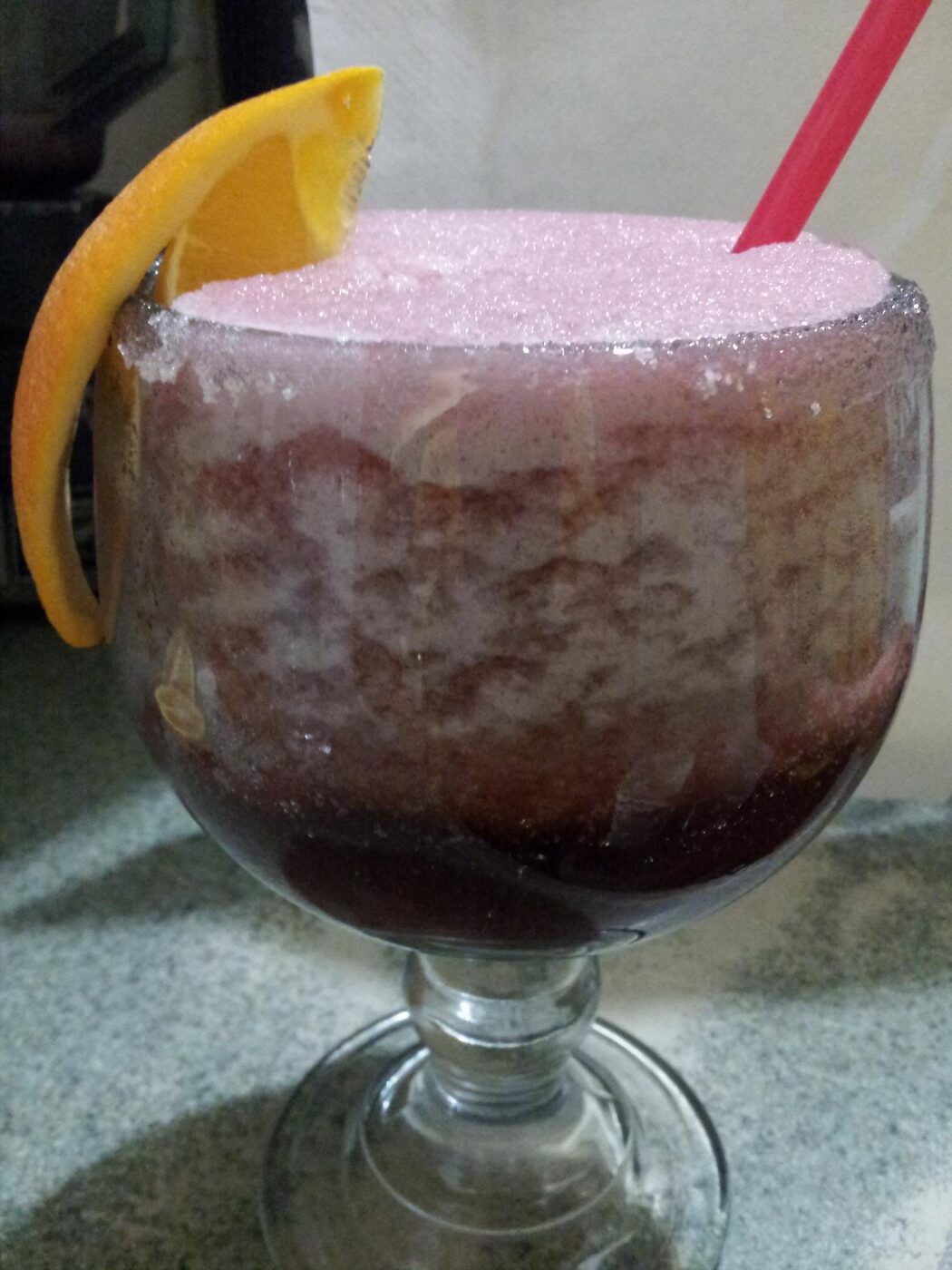 Colorful frozen margarita with a sugar rim and orange garnish